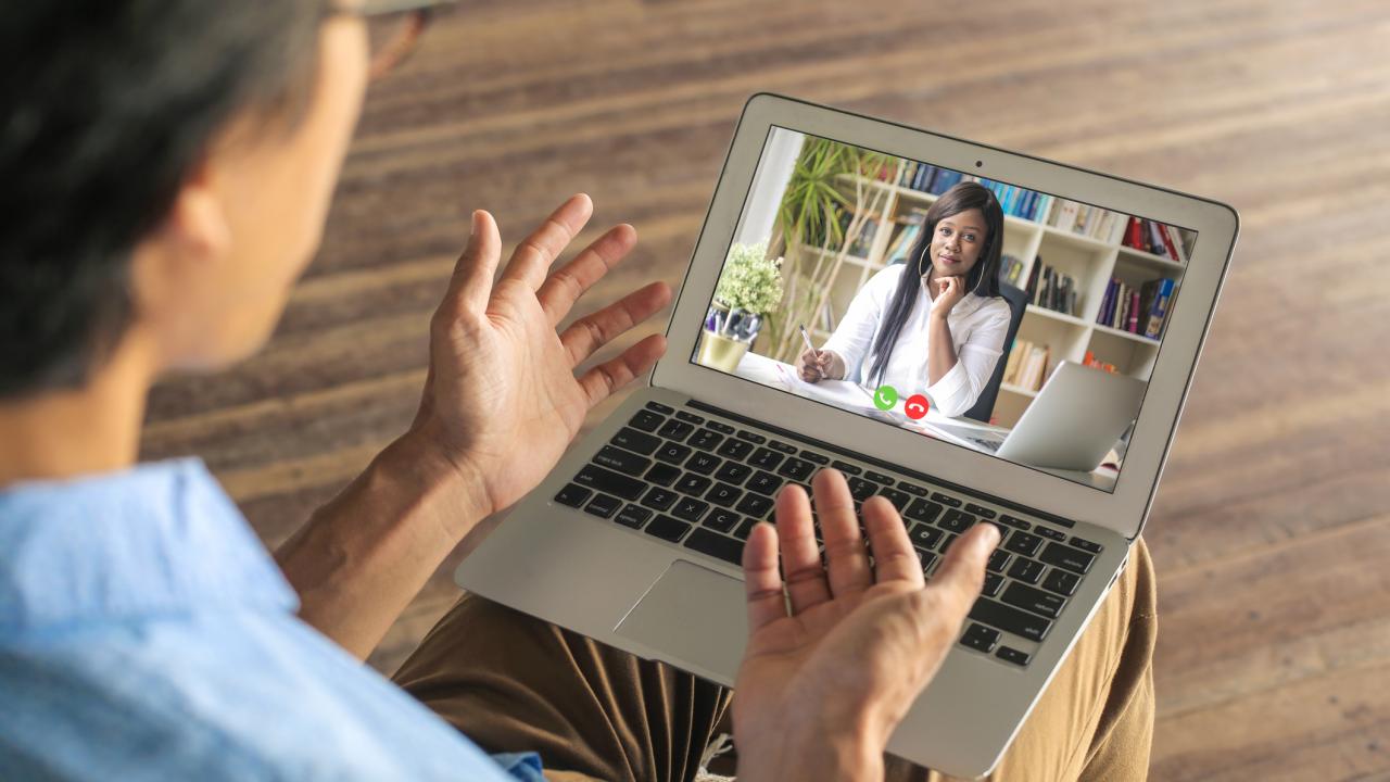 Man speaking to a woman via videoconference on a laptop.