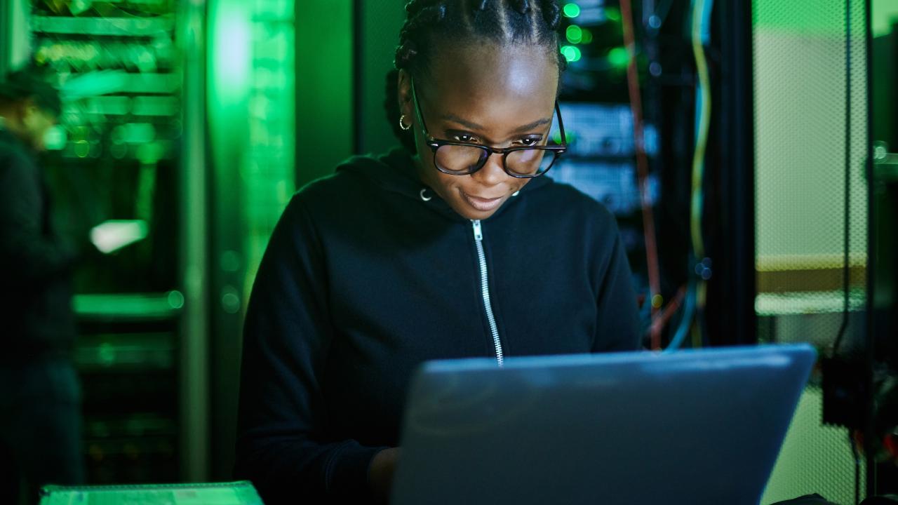 female computer programmer sitting at laptop in dark server room
